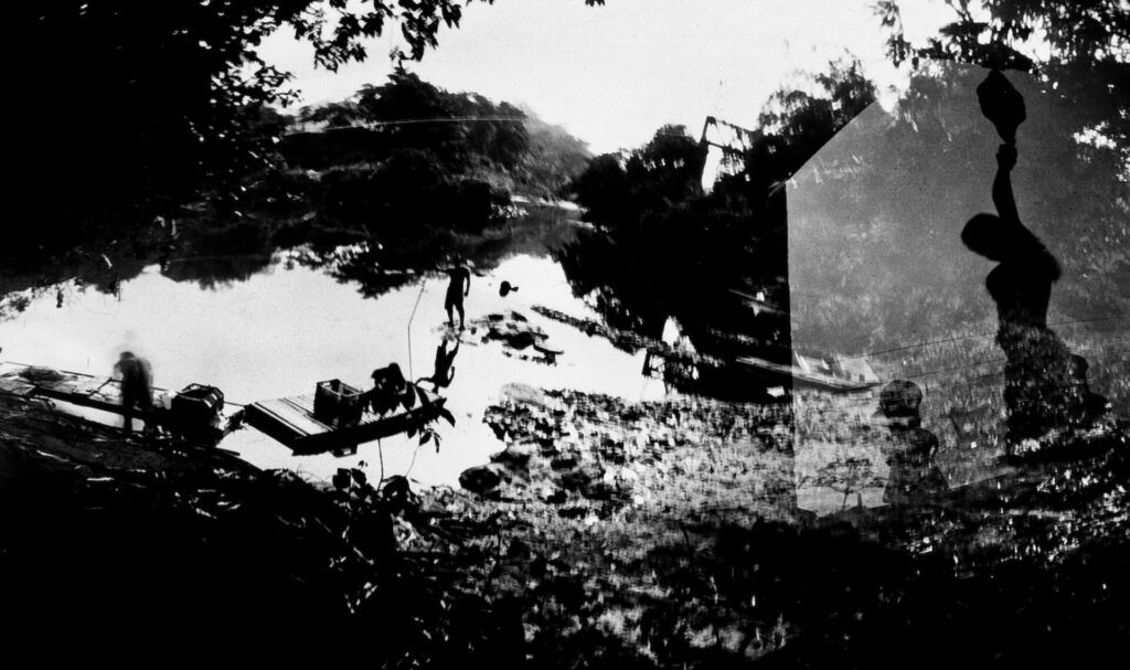 Fotografia paisagem, em diagonal direita, com sobreposição de fotos. Em um ambiente semelhante a um mangue, com lama e vegetação, são vistas duas pessoas. A da esquerda está com o corpo inclinado para baixo, próximo de duas canoas.  A da direita, um pouco mais afastada e tem uma vara na mão. De perto, mais para o canto direito, há uma imagem sobreposta de duas pessoas, semelhantes a uma criança e uma mulher. 