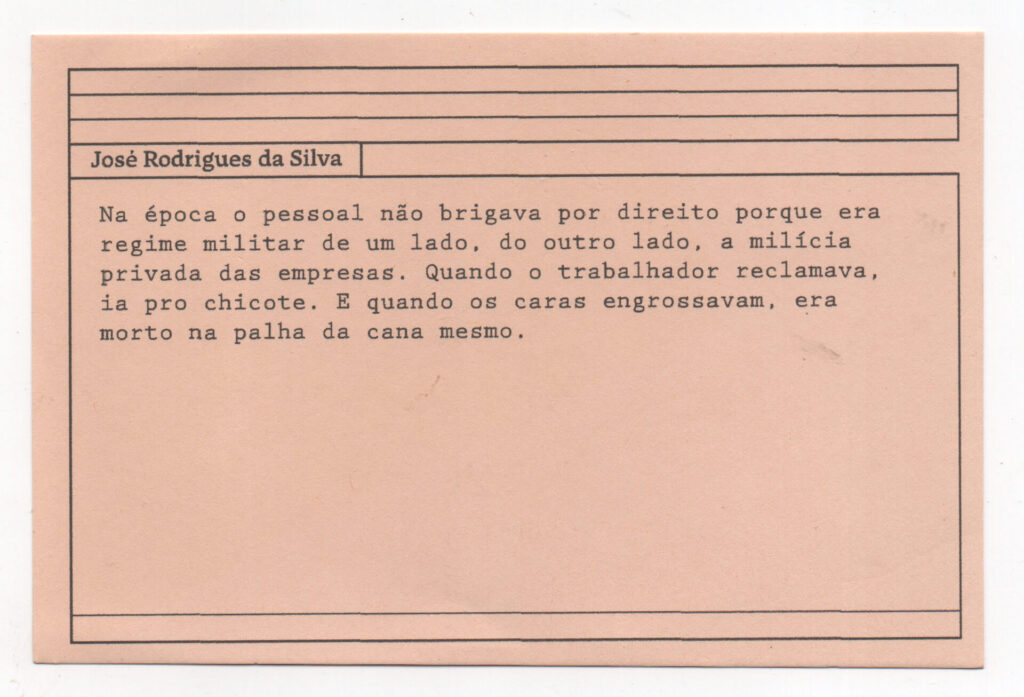 Fotografia de uma ficha horizontal cor de rosa claro com cinco pautas pretas na
parte superior. Abaixo delas, em letras pretas, o depoimento de José Rodrigues da
Silva, em letras pretas: “Na época, o pessoal não brigava por direito porque era
regime militar de um lado, do outro lado a milícia privada das empresas. Quando o
trabalhador reclamava, ia pro chicote. E quando os caras engrossavam, era morto
na palha da cana mesmo.” No rodapé, duas pautas pretas horizontais.