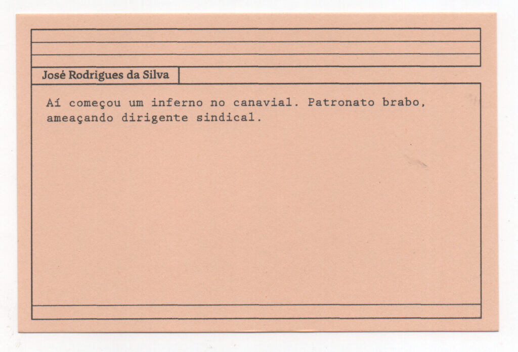 Fotografia de uma ficha horizontal cor de rosa claro com cinco pautas pretas na
parte superior. Abaixo delas, em letras pretas, o depoimento de José Rodrigues da
Silva, em letras pretas: “Aí começou um inferno no canavial. Patronato brabo,
ameaçando dirigente sindical.” No rodapé, duas pautas pretas horizontais.
