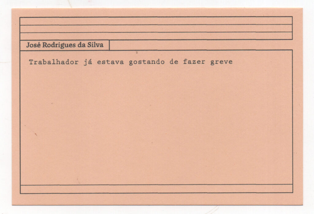 Fotografia de uma ficha horizontal cor de rosa claro com cinco pautas pretas na
parte superior. Abaixo delas, em letras pretas, o depoimento de José Rodrigues da
Silva, em letras pretas: “Trabalhador já estava gostando de fazer greve.” No rodapé,
duas pautas pretas horizontais.