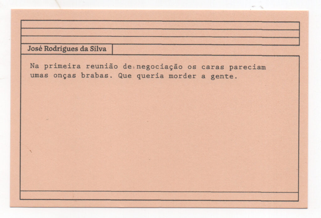 Fotografia de uma ficha horizontal cor de rosa claro com cinco pautas pretas na
parte superior. Abaixo delas, em letras pretas, o depoimento de José Rodrigues da
Silva, em letras pretas: “Na primeira reunião de negociação, os caras pareciam

umas onças brabas. Que queria morder a gente.” No rodapé, duas pautas pretas
horizontais.