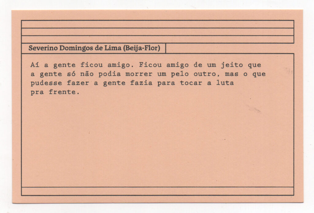 Fotografia de uma ficha horizontal cor de rosa claro com cinco pautas pretas na
parte superior. Abaixo delas, em letras pretas, o depoimento de Severino Domingos
de Lima (Beija-flor): “Aí a gente ficou amigo. Ficou amigo de um jeito que a gente só
não podia morrer um pelo outro, mas o que pudesse fazer a gente fazia para tocar a
luta pra frente.” No rodapé, duas pautas pretas horizontais.