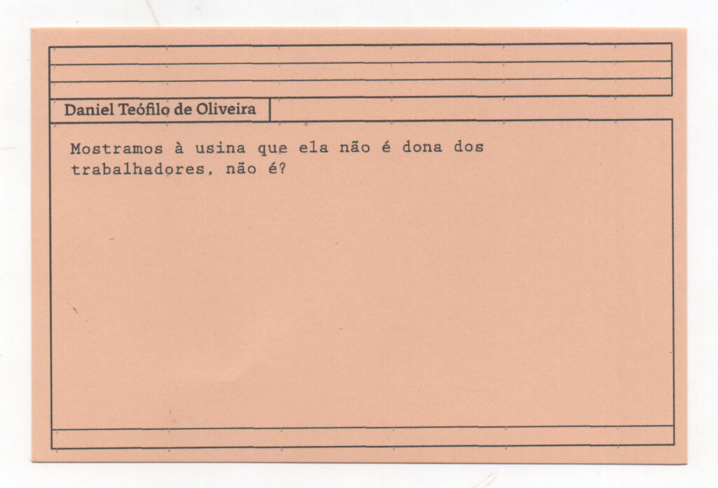 Fotografia de uma ficha horizontal cor de rosa claro com cinco pautas pretas na
parte superior. Abaixo delas, em letras pretas, o depoimento de Daniel Teófilo de
Oliveira: “Mostramos à usina que ela não é dona dos trabalhadores, não é?” No
rodapé, duas pautas pretas horizontais.