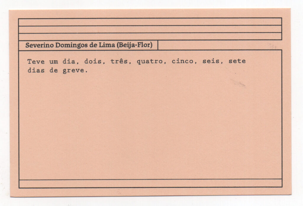 Fotografia de uma ficha horizontal cor de rosa claro com cinco pautas pretas na
parte superior. Abaixo delas, em letras pretas, o depoimento de Severino Domingos
de Lima (Beija-Flor): “Teve um dia, dois, três, quatro, cinco, seis, sete dias de
greve.” No rodapé, duas pautas pretas horizontais.