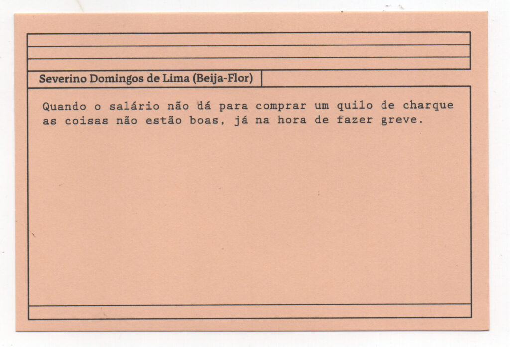 Fotografia de uma ficha horizontal cor de rosa claro com cinco pautas pretas na
parte superior. Abaixo delas, em letras pretas, o depoimento de Severino Domingos
de Lima (Beija-Flor): “Quando o salário não dá para comprar um quilo de charque as

coisas não estão boas, já na hora de fazer greve. No rodapé, duas pautas pretas
horizontais.