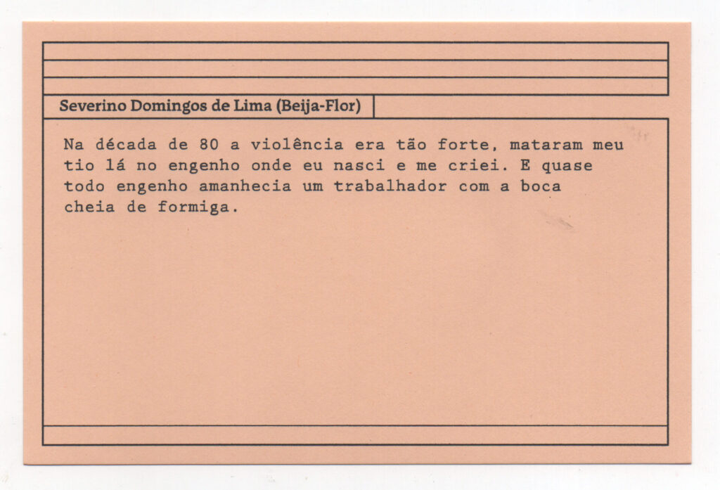 Fotografia de uma ficha horizontal cor de rosa claro com cinco pautas pretas na
parte superior. Abaixo delas, em letras pretas, o depoimento de Severino Domingos
de Lima (Beija-Flor): “Na década de 80 a violência era tão forte, mataram meu tio lá
no engenho onde eu nasci e me criei. E quase todo engenho amanhecia um
trabalhador com a boca cheia de formiga.” No rodapé, duas pautas pretas
horizontais.