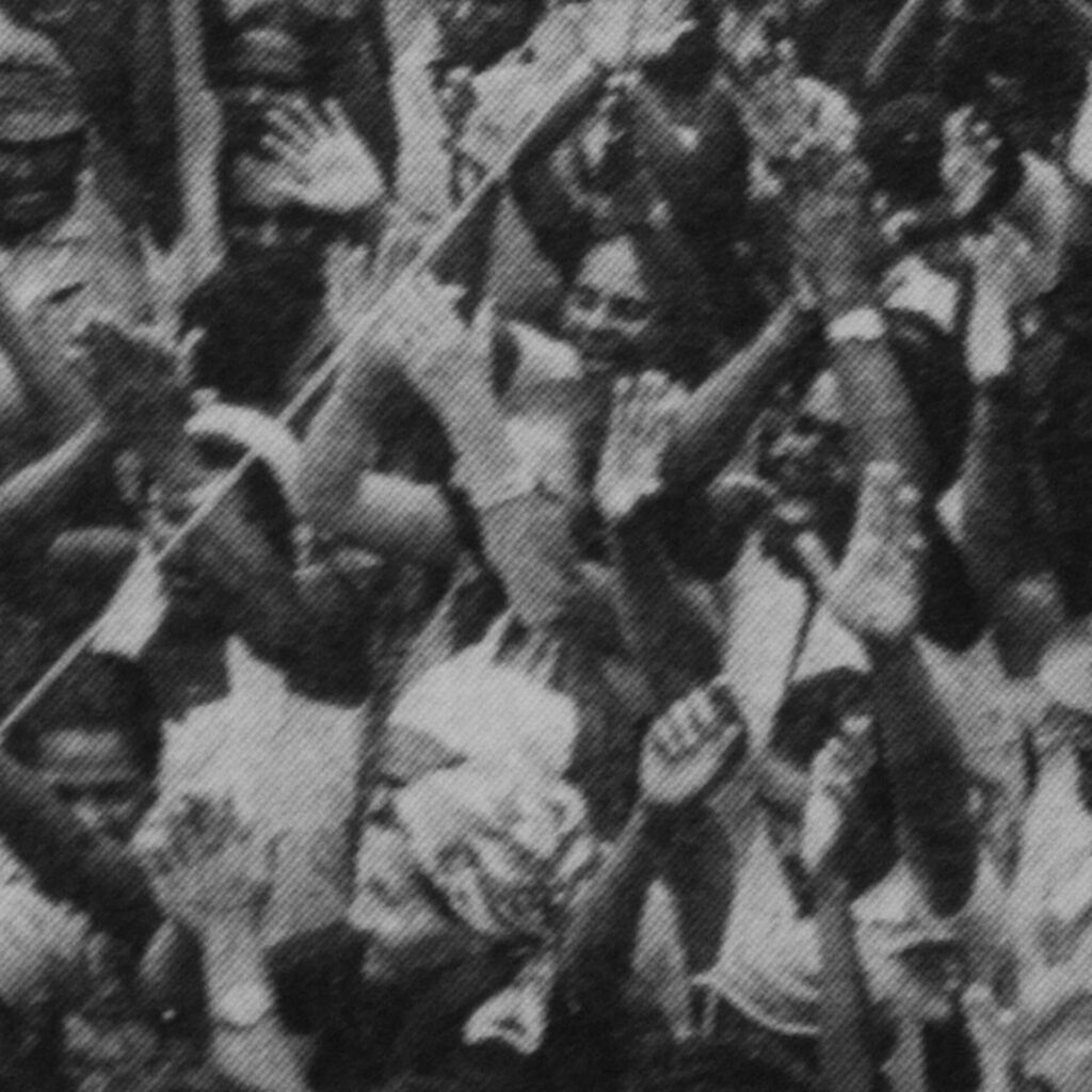 Foto de uma fotografia antiga em preto e branco na vertical. Trabalhadores rurais
em greve olham para a frente e aplaudem. Alguns estão com a boca aberta, como
se gritassem ou cantassem.